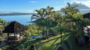 A tropical resort with a pool, palm trees, and a view of a lake and a mountain. - Wide Luxury Home with Pool & Jacuzzi access & Amazing Volcano and Lake views (El Castillo)