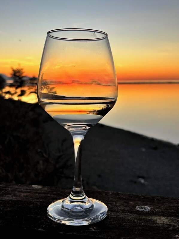 A clear glass of water on a wooden surface with a sunset in the background. - Waterfront Studio Private Guest Suite at Dungeness Barn House (Sequim)