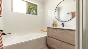 Un baño moderno con una bañera, un tocador con espejo y una ventana con vistas a árboles.