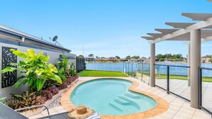 A swimming pool with a curved edge, surrounded by a tiled deck and a pergola. - Nirvana Waters - Absolute Waterfront Escape with Private Pontoon & Pool - Holiday Yamba (YAMBA)