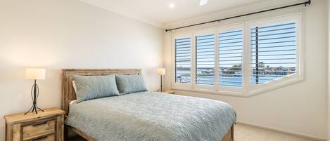 Ein Schlafzimmer mit einem Bett, zwei Nachttischen, einem Hängeventilator und einem großen Fenster mit Blick auf ein Gewässer.