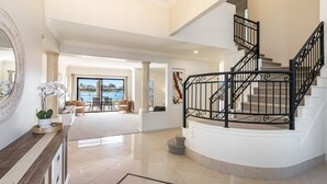 A spacious living area with a view of a body of water, a curved staircase with black railings, and a large mirror on the left. - Nirvana Waters - Absolute Waterfront Escape with Private Pontoon & Pool - Holiday Yamba (YAMBA)