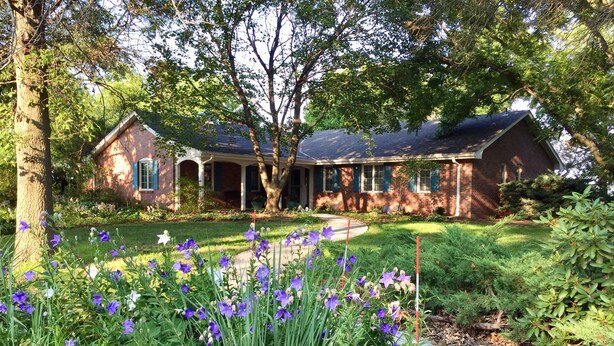 A brick house with a covered porch and a well-maintained garden with purple flowers.