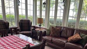 A cozy living room with a brown leather sofa, plaid armchairs, and a red and white checkered table.