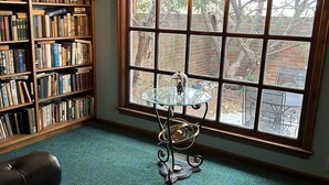 A room with a large window, a bookshelf, a table with a glass top, and a leather chair.