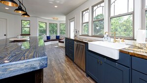 Una cocina con una isla grande, armarios oscuros y vistas a zonas verdes por las ventanas.