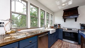 Una cocina con armarios azul oscuro, lavavajillas de acero inoxidable, horno empotrado y un amplio ventanal con vistas a zonas verdes.