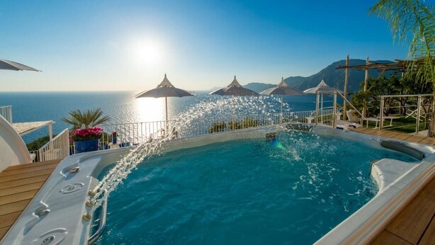 Een hottub met uitzicht op zee en bergen, omringd door parasols en ligbedden.