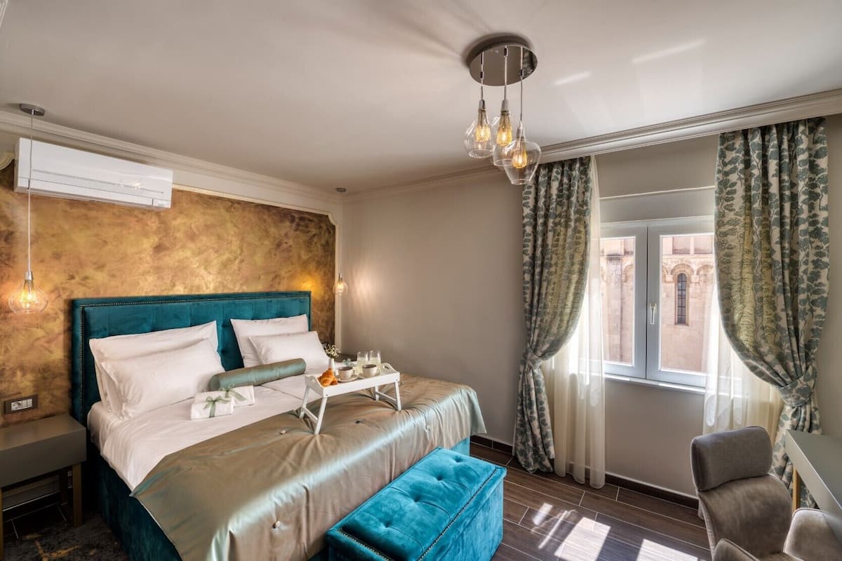 A hotel room with a bed, bedside table, and a window with curtains.