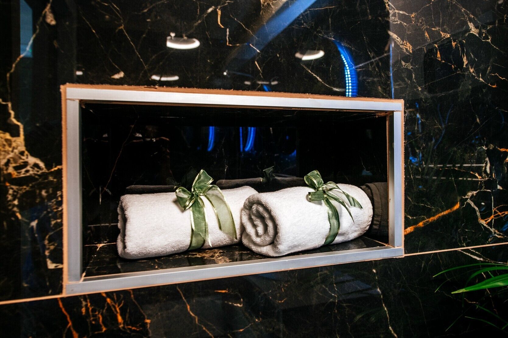A framed display of two neatly rolled towels tied with green ribbons, set against a dark marble background.