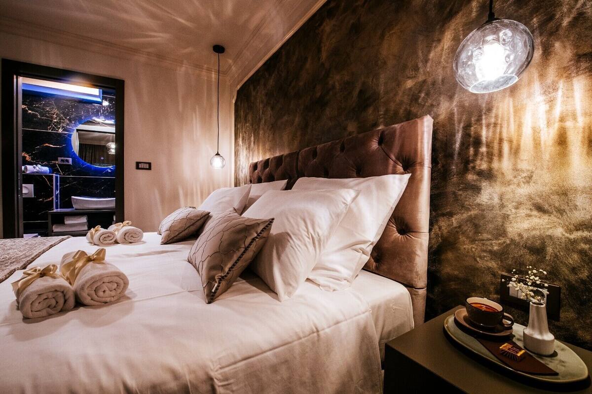 A hotel room with a large bed, a headboard, a nightstand with a tray of amenities, and a wall-mounted light.