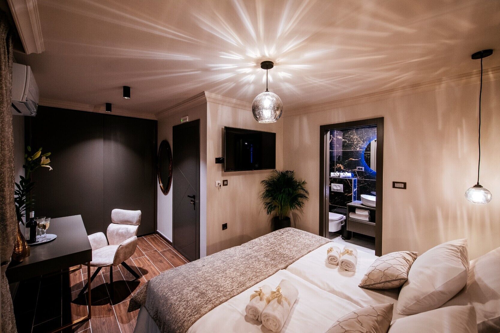 A modern hotel room with a large bed, a desk, a chair, a TV, and a bathroom with a marble backsplash.