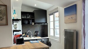 Une cuisine de taille réduite avec une table en bois, une chaise noire et un réfrigérateur.