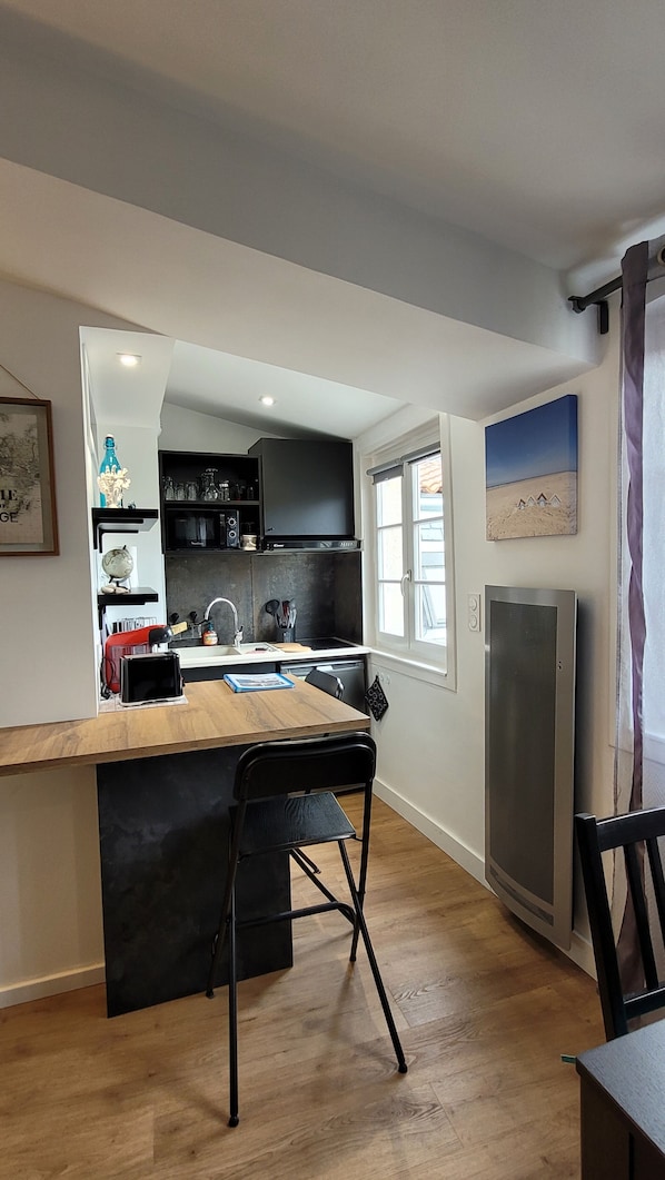 A compact kitchen with a wooden table, a black chair, and a refrigerator.