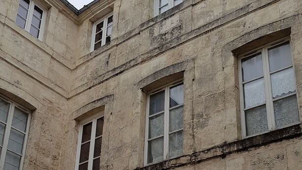 Un immeuble à plusieurs étages, doté d’une façade usée par le temps, de nombreuses fenêtres et d’une porte.