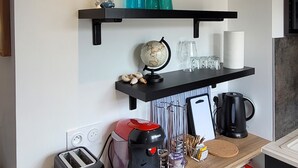Une cuisine moderne avec un plan de travail noir, une machine à café Bosch, un grille-pain et une étagère suspendue agrémentée d’objets décoratifs.