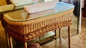 Uma mesa de vime com tampo de vidro, uma miniatura de veleiro e uma cesta trançada.