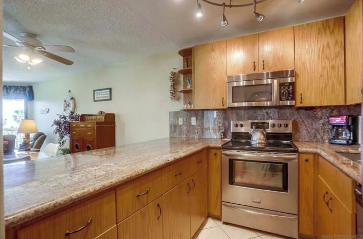 A kitchen with wooden cabinets, a granite countertop, stainless steel appliances, and a ceiling fan.