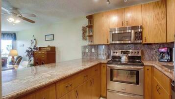 A kitchen with wooden cabinets, a granite countertop, stainless steel appliances, and a ceiling fan.