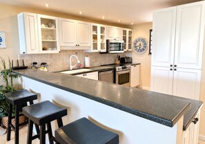 A modern kitchen with white cabinets, a granite countertop, a built-in oven, and a microwave.