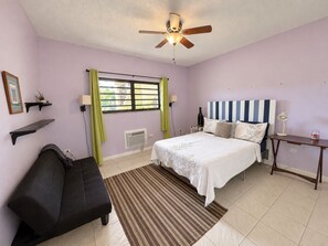 A bedroom with a bed, a nightstand, a desk, a chair, a ceiling fan, and a window with curtains. - 3 Bedroom, 3 Bath Oceanfront Condo  (Christiansted)