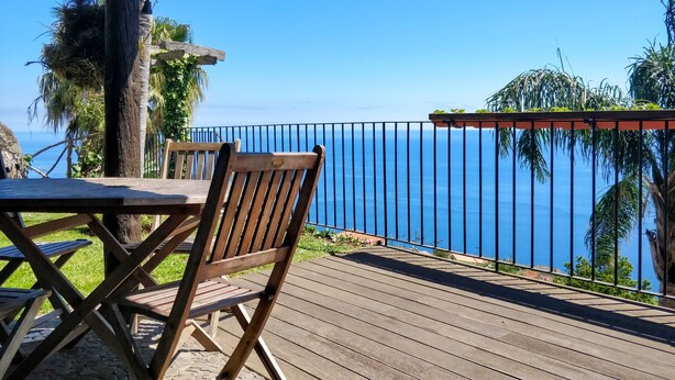 A wooden deck with a table and chairs, overlooking a clear blue sea.