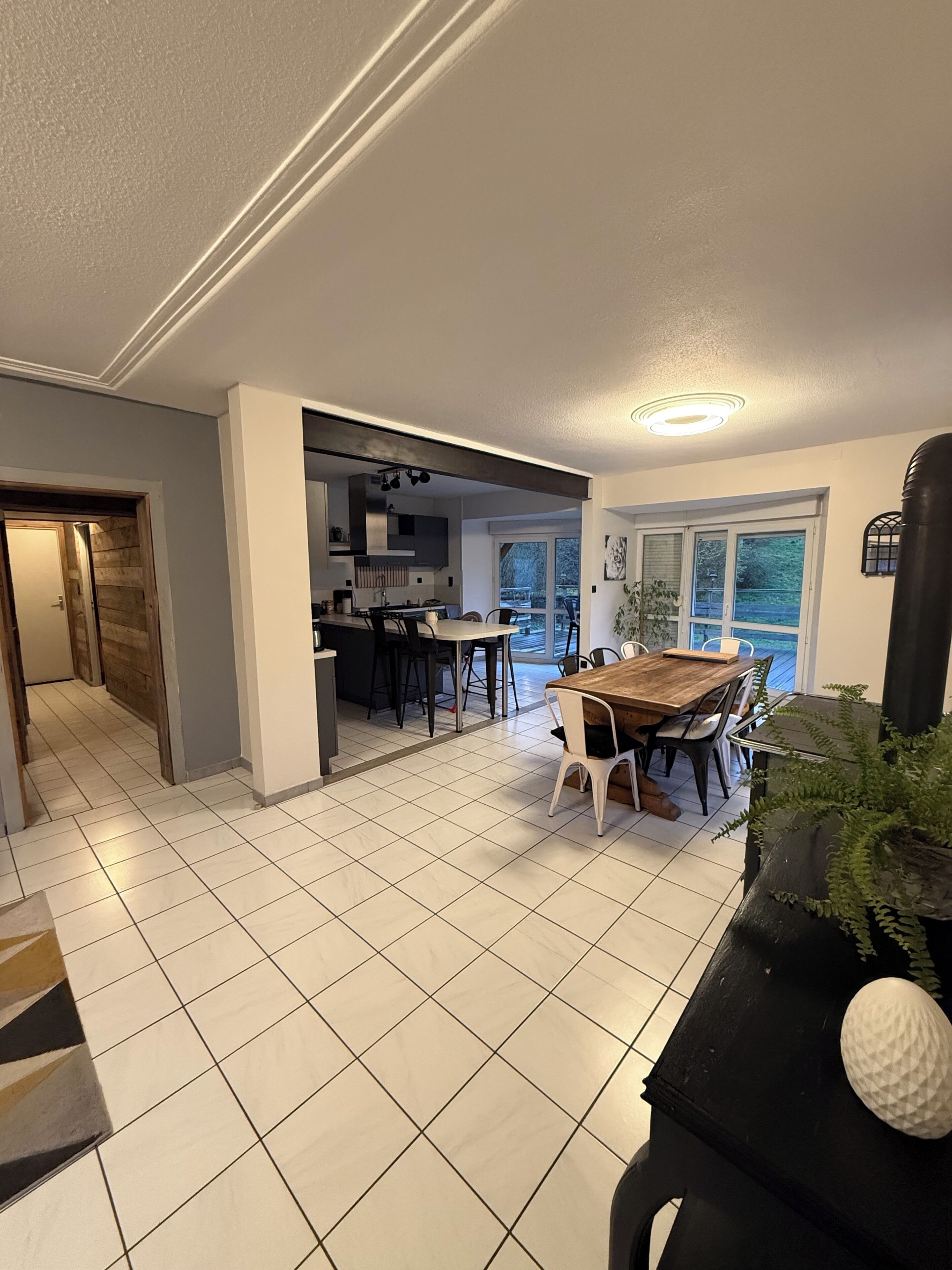 A modern kitchen with a dining area, large windows, and a view of the outdoors.
