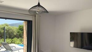 Ein modernes Hotelzimmer mit einem großen Bett, einem an der Wand montierten Fernseher und Blick auf einen Swimmingpool und Grünflächen.