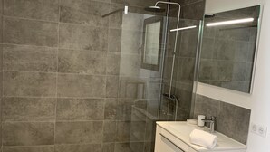 Ein modernes Badezimmer mit einer gläsernen Duschkabine, einem weißen Waschtisch mit Spiegel und einem Handtuch auf dem Boden.