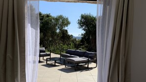 Ein Schlafzimmer mit Bett, Blick auf eine Terrasse mit Tisch und Stühlen und transparenten Vorhängen.