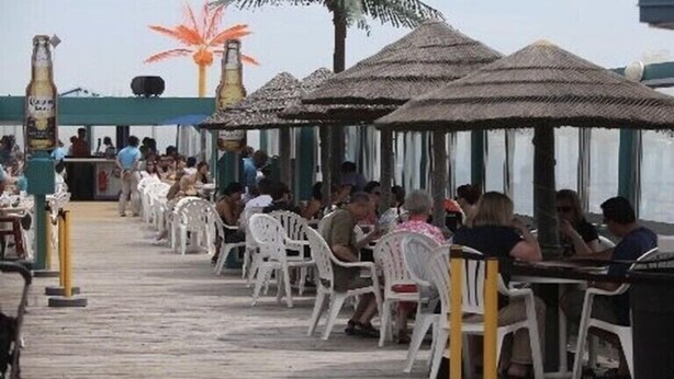 Un restaurante frente al mar con mesas al aire libre, sombrillas de paja y vistas del océano.