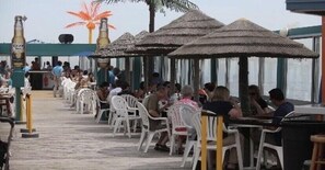 Un restaurante frente al mar con mesas al aire libre, sombrillas de paja y vistas del océano.