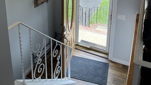 Una escalera con barandilla blanca, un candelabro y una puerta que da al exterior.