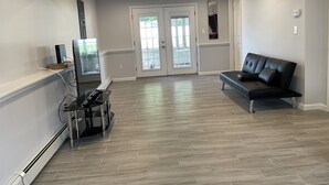 Una sala de estar moderna con un sofá de cuero negro, una mesa de centro de vidrio y un televisor de pantalla plana sobre un mueble.