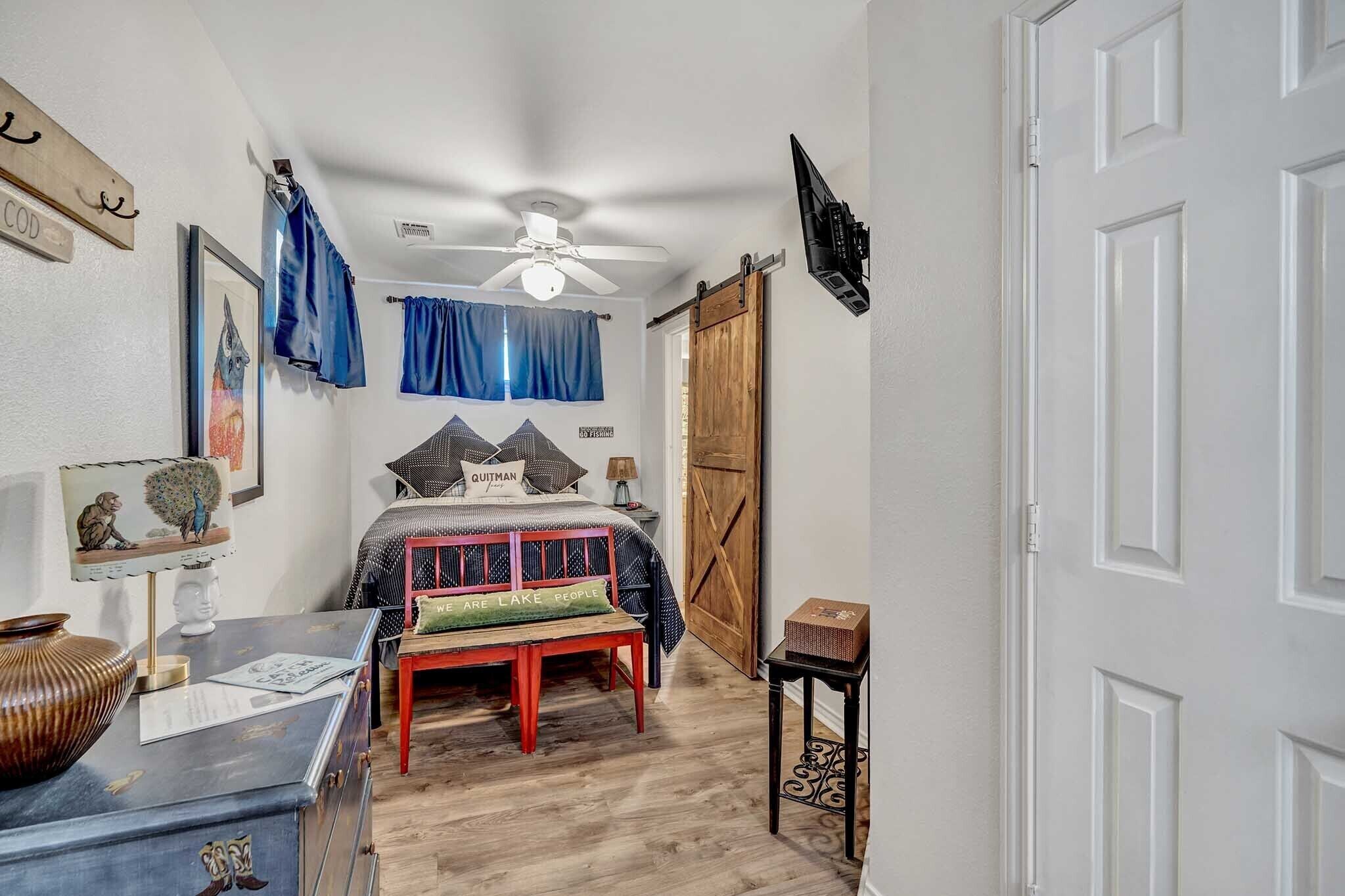 A bedroom with a bed, a desk, a chair, a ceiling fan, a wardrobe, and a door.