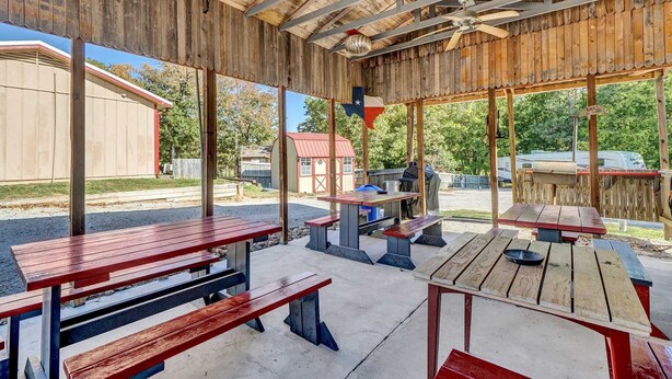 An outdoor patio with wooden tables and benches, a grill, and a Texas flag. - Crappie Cabin - Room 5 (Wood County)