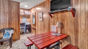 A compact room with wooden walls, a television mounted on the wall, a small table with a lamp, and a chair with a pillow. - Crappie Cabin - Room 5 (Wood County)