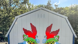 A wooden shed with a mural of two colorful fish on its side. - Crappie Cabin - Room 5 (Wood County)