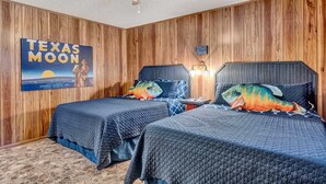 Una habitación con paneles de madera, dos camas con ropa de cama azul, un ventilador de techo y un cartel de Texas Moon.