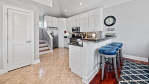 Una cocina moderna con armarios blancos, una isla central con taburetes y un refrigerador de acero inoxidable, además de un microondas.