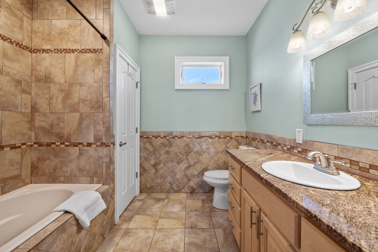A bathroom with a bathtub, toilet, sink, and a window.