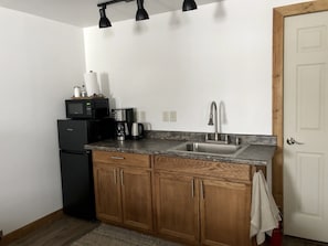 Cocina compacta con refrigerador, cafetera, microondas y pileta.