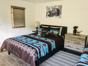 Une chambre à coucher comprenant un lit, une table de chevet, une commode, une fenêtre avec des stores et un tableau accroché au mur.