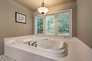 Ein Badezimmer mit einer großen Badewanne, einer gerahmten Karte an der Wand und drei Fenstern mit Jalousien.