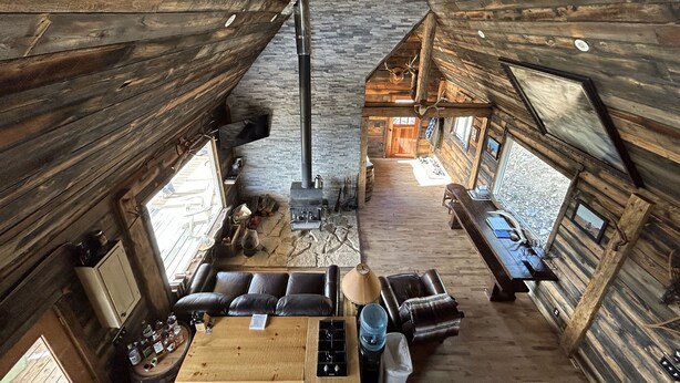 L’intérieur d’un chalet rustique, avec une cheminée en pierre, des murs en bois et un coin salon accueillant.