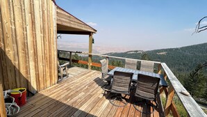 Une terrasse en bois avec une table et des chaises, offrant une vue sur un paysage montagneux.