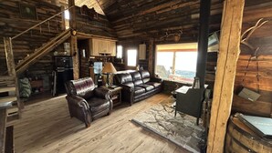 L’intérieur d’un chalet rustique, avec un escalier en bois, un canapé en cuir et une cheminée en pierre.