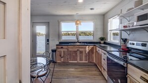 A kitchen with wooden cabinets, a black countertop, a stove, and a window overlooking a body of water. - Cozy new cabin on Lac Courte Oreilles!! (Hayward)