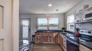 Une cuisine avec des meubles en bois, un plan de travail noir, une cuisinière et une fenêtre donnant sur un plan d’eau.