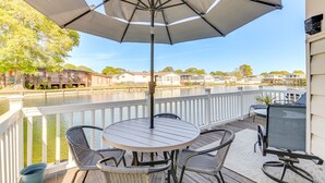 Una terraza con mesa y sillas, con vista a un cuerpo de agua y casas al fondo.